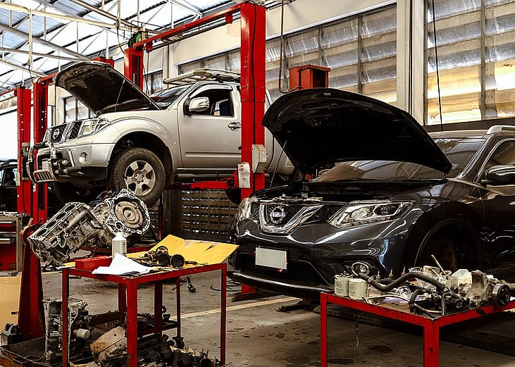 Cars seen on lifts with tools scattered around inside an automotive maintenance and repair shop.