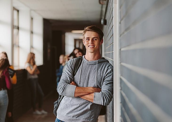 A young male university student standing and leaning to a wall in college corridor.