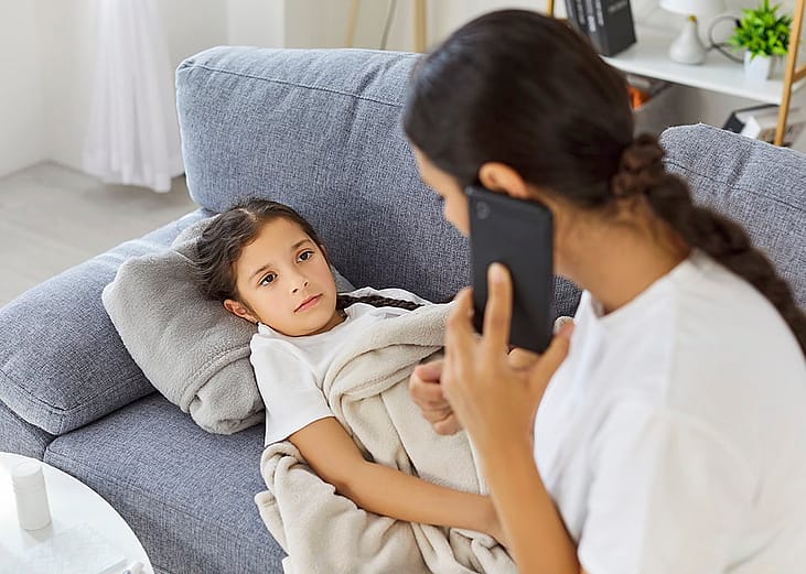 A mother taking care of her sick young daughter at home while making a phone call to her school.