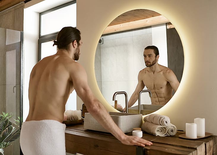 Man looking at himself in bathroom mirror while doing morning routine.