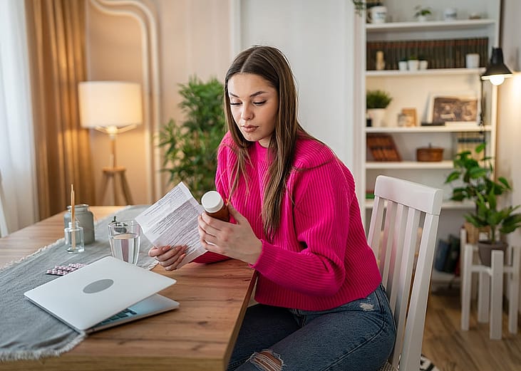 A young woman at home reading hospital bills and prescriptions.
