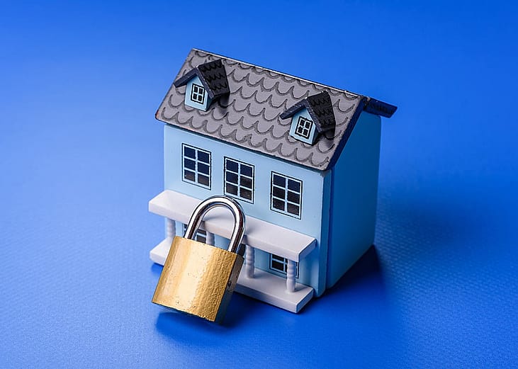 A small figure of a house with a golden padlock as a concept of home security.