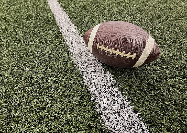 An American football seen on an artificial grass next to a white yard line.