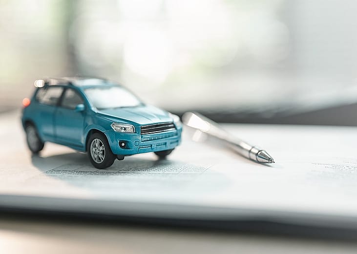 A miniature car and a pen placed above a sale contract, representing vehicle purchase through loan financing.