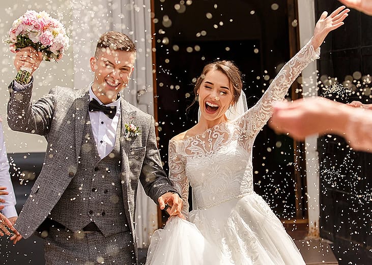 A newlywed couple celebrating after the ceremony while guests shower them with confetti.