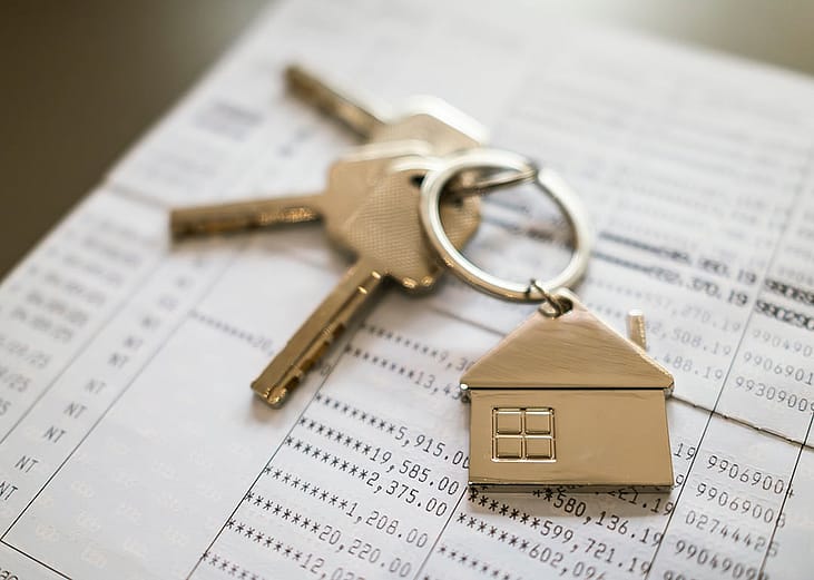 A keychain, house keys, and a bankbook in the background, representing a financial concept of cash flow for a home loan.