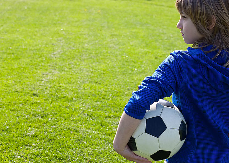 A young boy holding a soccer ball in a park field.