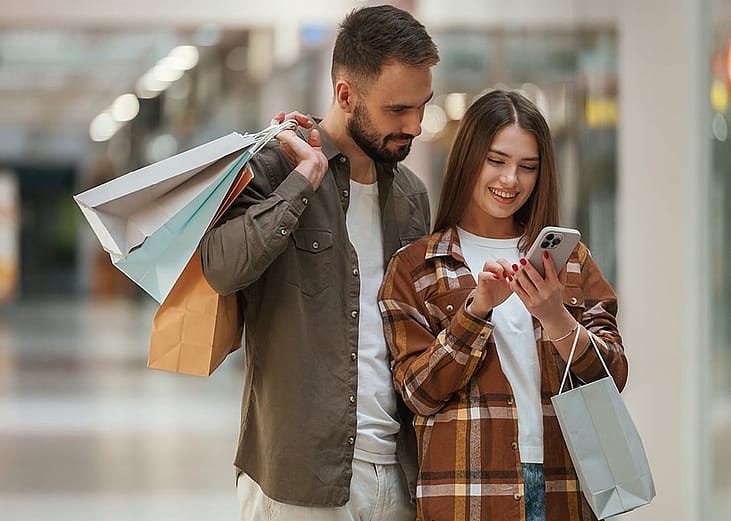 A young couple checking online special deals from a smartphone after shopping at the mall.