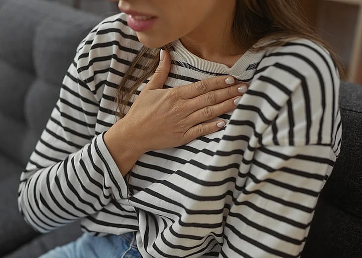 A person experiencing a heartburn with her hand pressed on the chest at home.