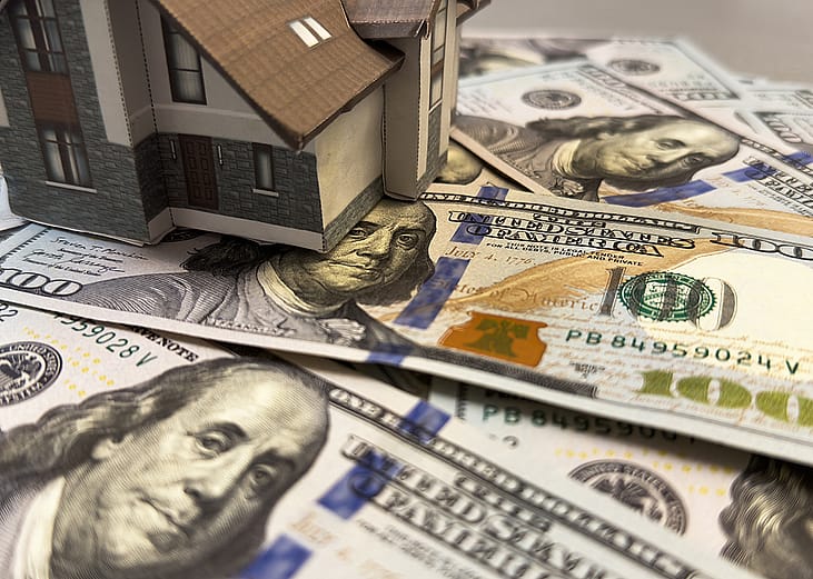 A miniature house above U.S. dollar bills, representing home equity and housing on credit concepts.