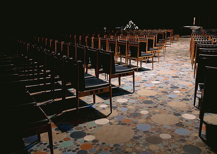 The interior of the Kaiser Wilhelm Memorial Church in Berlin, Germany, featuring rows of dark wood chairs.