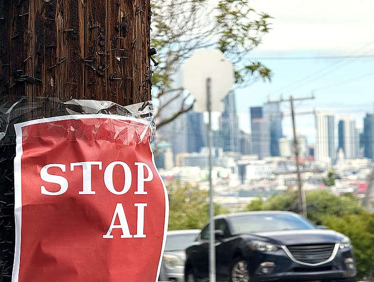 A red protest poster with a 'Stop AI' message taped to a wooden pole in a street.