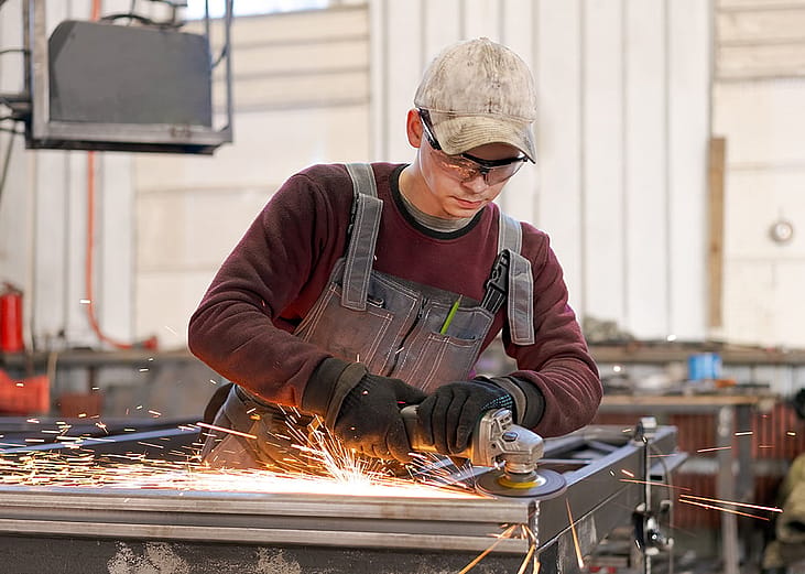 A worker wearing safety glasses while using an angle grinder on steel construction.