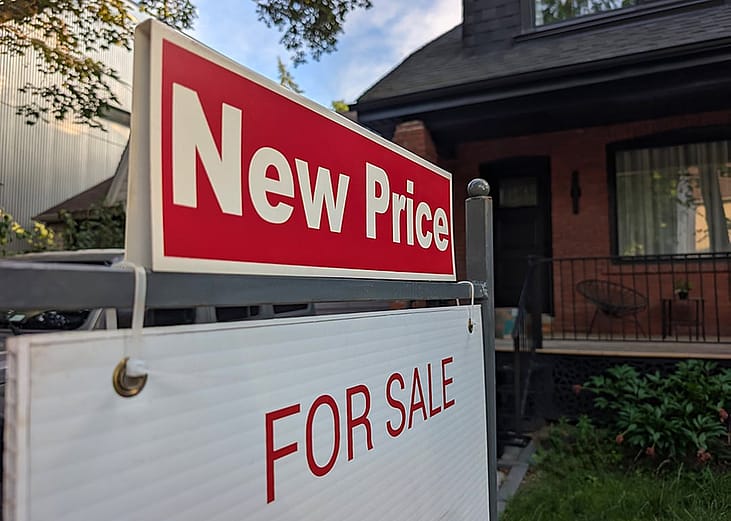 A sign for a new price sale displayed in a front yard of a single-detached residential house. 