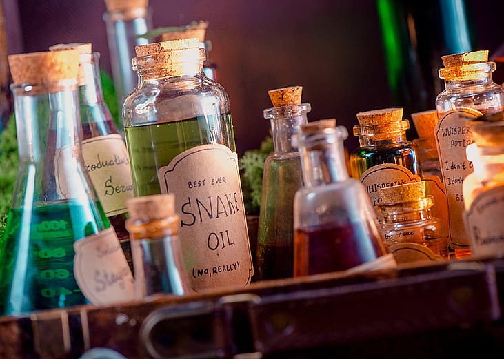 A collection of vintage-style glass bottles with potion and unscientific labels placed in a rustic tray.