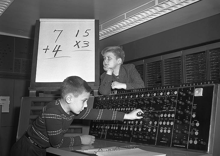 A black-and-white photo of two young boys who ponder at their homework on the electronic calculator at IBM's Watson Laboratory.