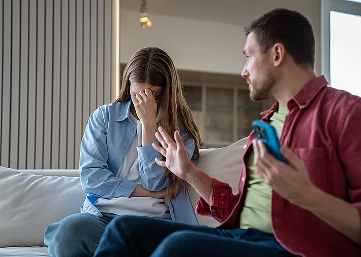 An upset woman sits in distress beside her angry husband.