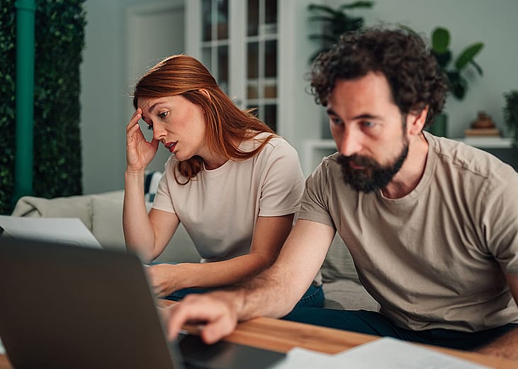 A couple at home feeling worried and stressed while calculating expenses.