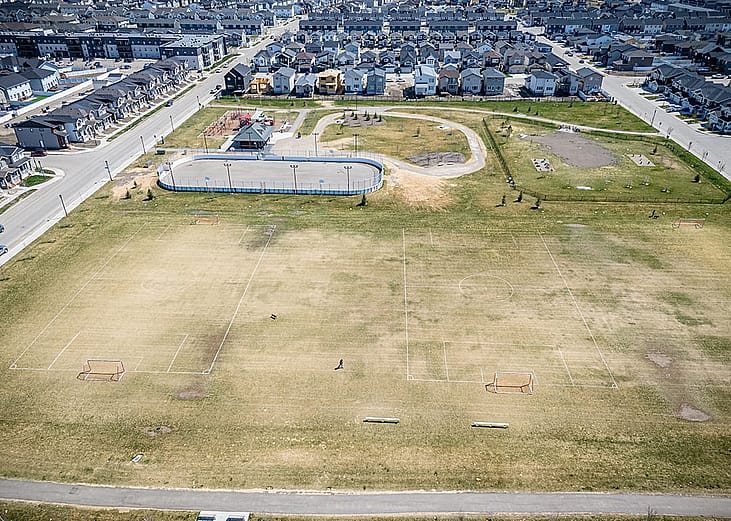 Aerial view of a large, open field in the foreground with lined soccer pitches and goals.