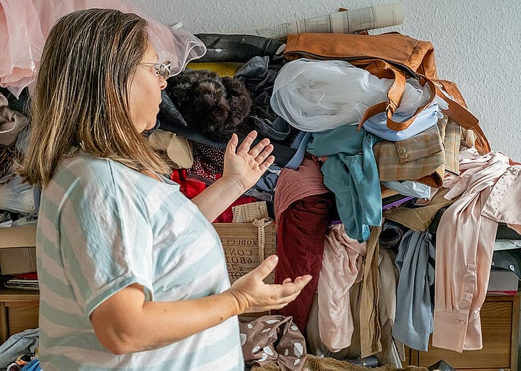 A person standing before a disorganized pile of mixed clothes at home.
