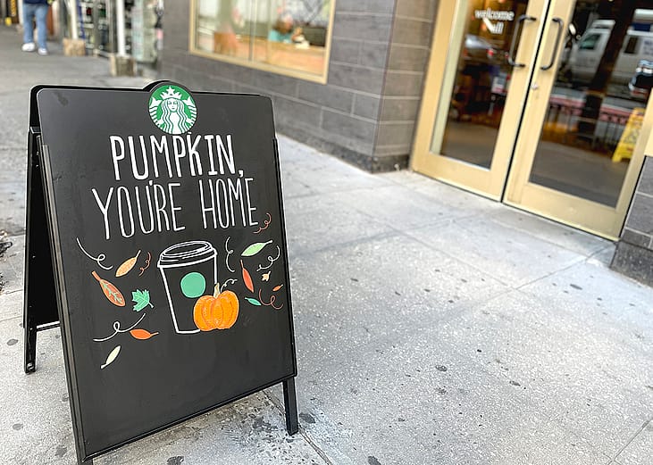 A Starbucks 'Pumpkin, you're home' sign on the sidewalk announcing Pumpkin Spice drinks are available at the store.