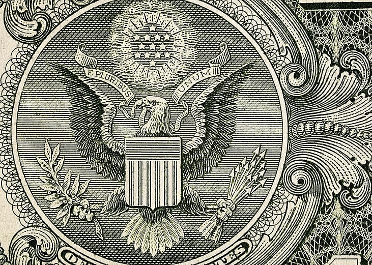 A close-up shot showing the macro details with the engraved eagle, shield, stars, and ornamental line work of the Great Seal of the United States on the one-dollar banknote.