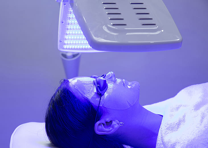 A young woman having blue LED light facial therapy.