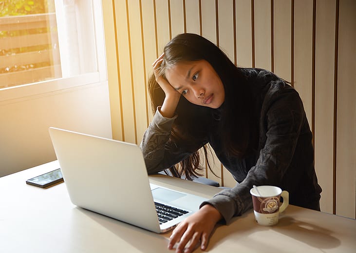 A female student looking anxious reviewing school reports on a laptop.
