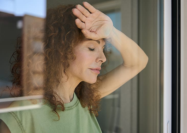 A woman leaning on a glass window experiencing fatigue.