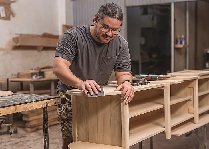 A woodworker using a sandpaper to smoothen the edges of a new shoe bench at his furniture workshop.