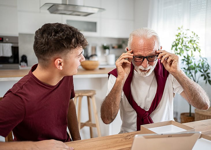 Senior man trying new eyeglasses with his grandson helping him at home.
