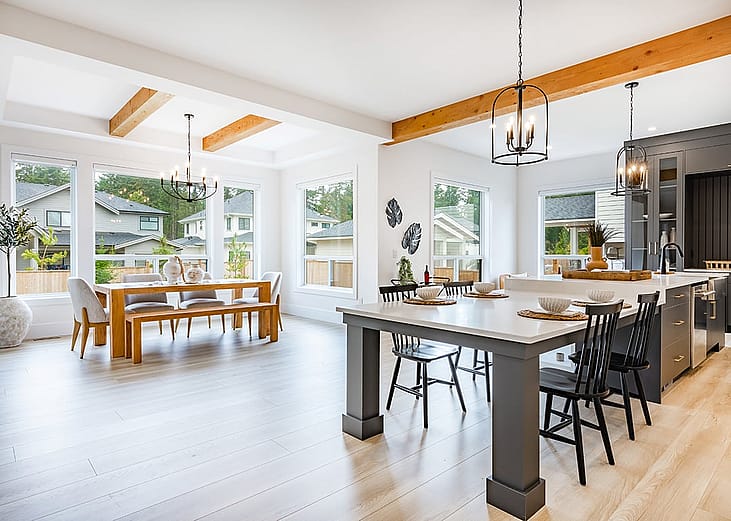 An interior of a modern home's living area, dining, and kitchen with its large glass windows.