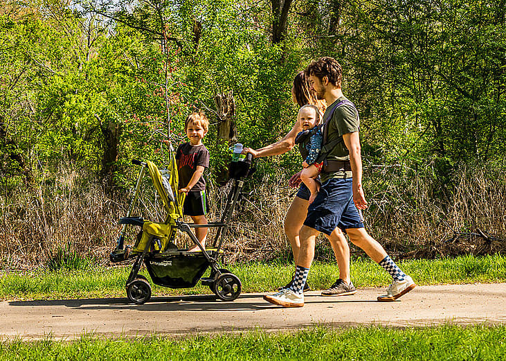 A young family walking at the park with a stroller.