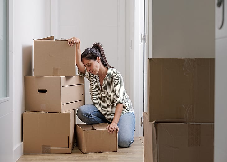 A person crouching on the floor from exhaustion after carrying heavy and large boxes into her new apartment.