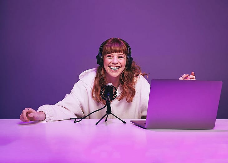 A happy young woman laughing while recording a live radio show in a studio.