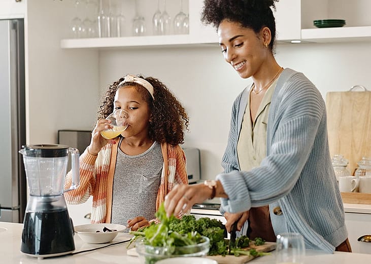 A mother prepares food with her young daughter in the kitchen.
