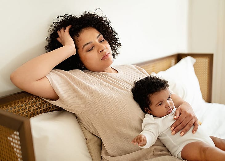 A parent resting her head on the wall while making the baby fall asleep in a bedroom.