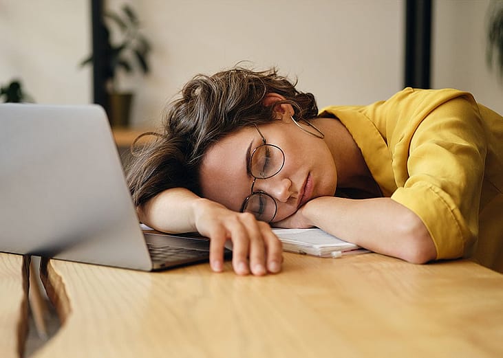 A tired young woman sleeping on a desk at work.