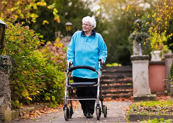 A senior woman pushing her walker while walking in a park.