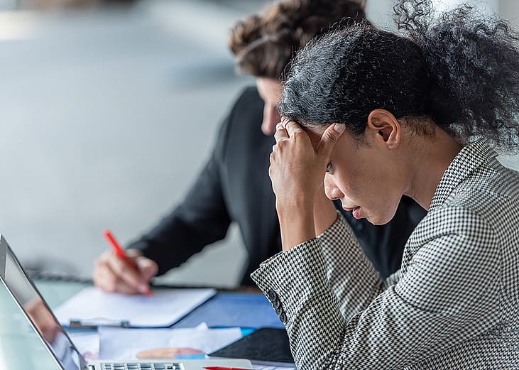 An employee looking stressed during a work process review with a colleague in the office.