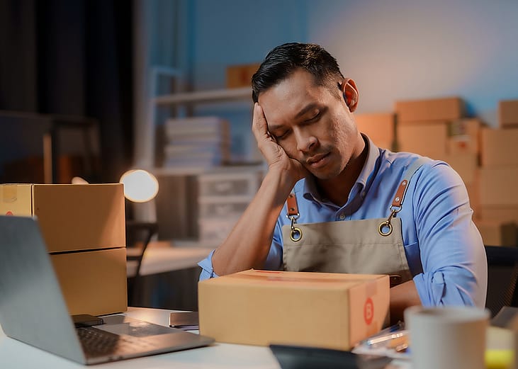 A stressed small business owner falling asleep while packing orders as a concept of a struggling business.
