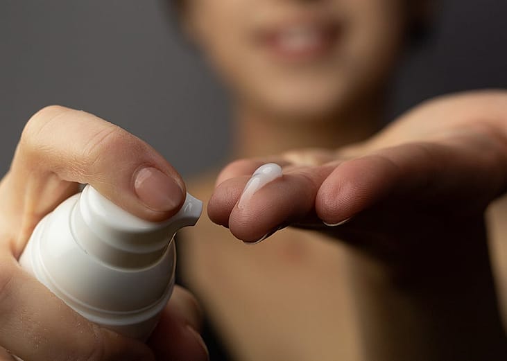A closeup of a young adult putting prescription retinoid first to her finger then to her face.