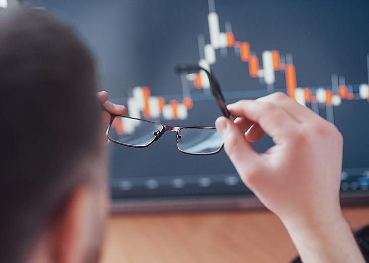 A businessman holding his glasses up against stock charts to review in an office.