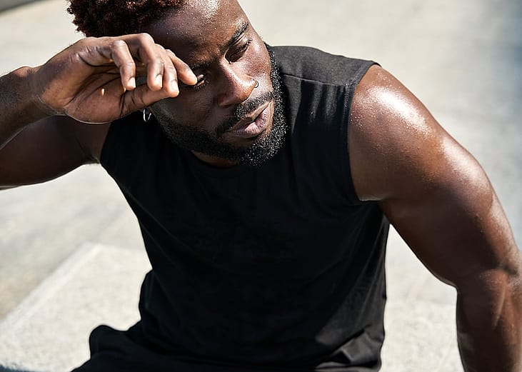 A fit young man in sportswear sweating after a workout in a park.