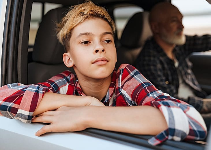 A young boy looking out the car window with his father driving the car.