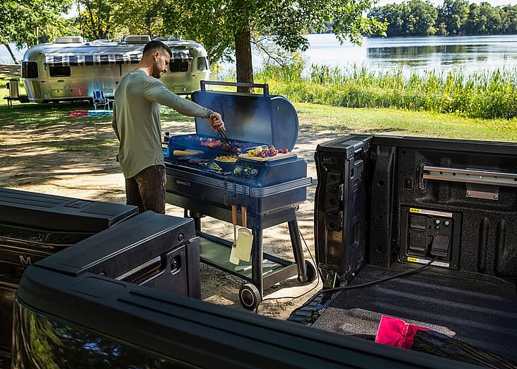 A man grills food on a portable barbecue powered by the Pro Power Onboard feature in the bed of a 2026 Ford F-150.