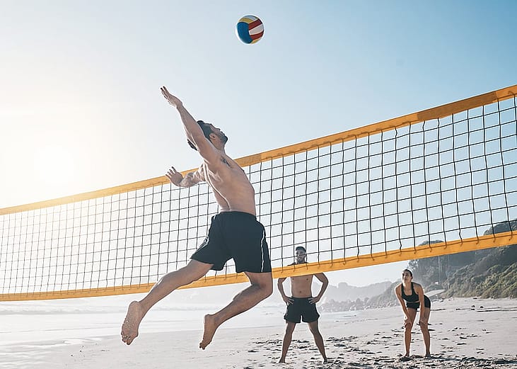 A person jumping for the ball during a beach volleyball match with friends.