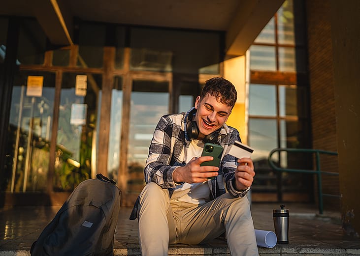 A university student using his smartphone and credit card for online shopping.