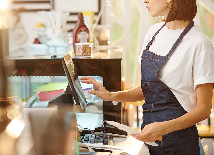 A female barista working at the counter of a coffee shop.