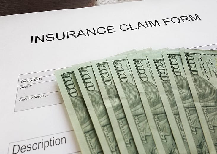 An insurance claim form and U.S. dollar bills placed above the blank document.